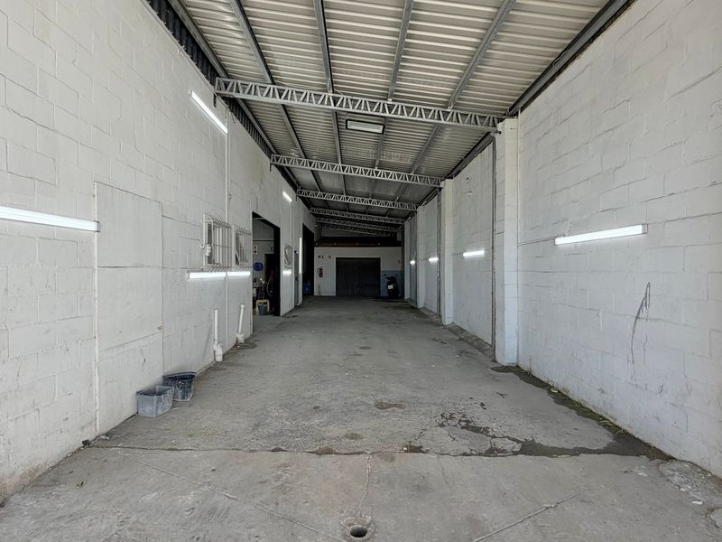 Spacious industrial utility area featuring exposed steel roof trusses, concrete block walls, and durable concrete flooring with integrated lighting.
