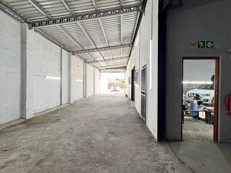Spacious industrial utility area featuring exposed steel roof trusses, concrete block walls, and functional strip lighting, suitable for storage or workshop use.