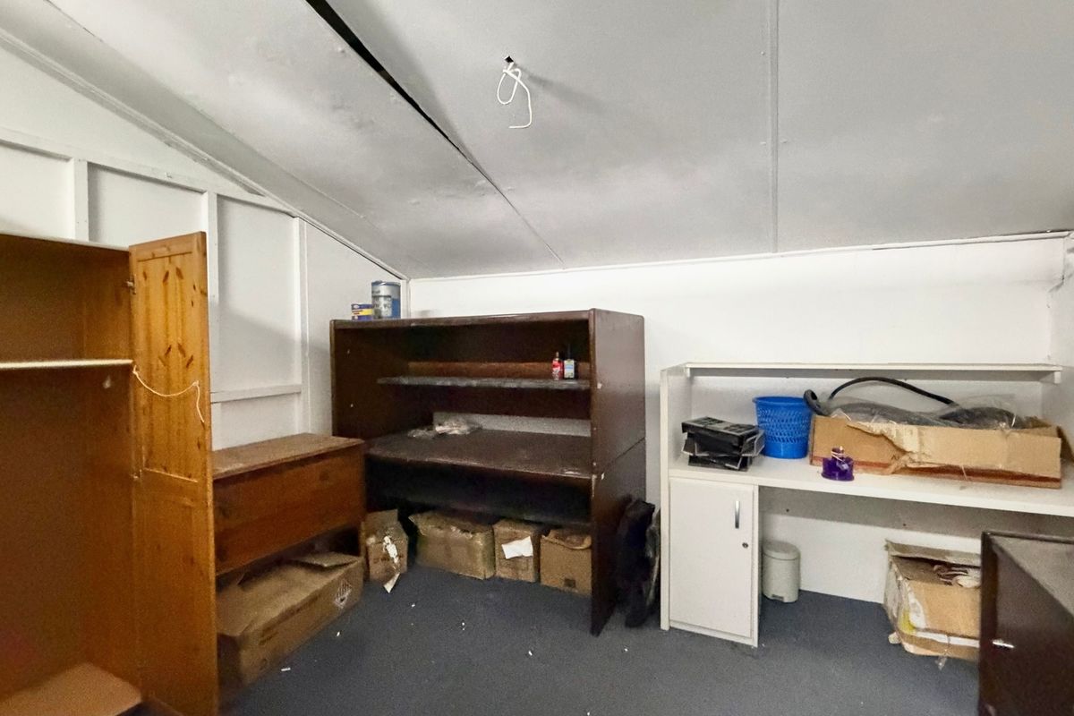 A utility space featuring a sloped ceiling with exposed wiring, suitable for storage or workshop use, requiring maintenance and cosmetic updates.