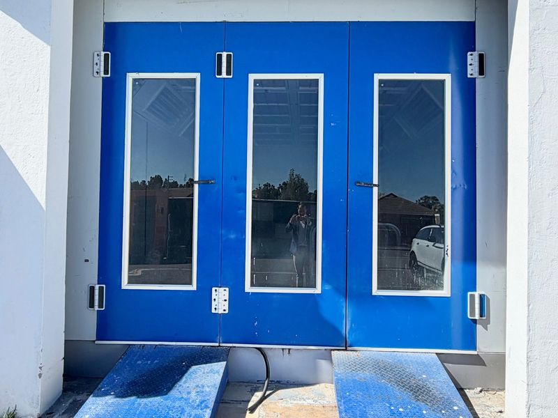 Industrial entrance featuring blue double doors with glass panels and integrated metal loading ramps for commercial access.