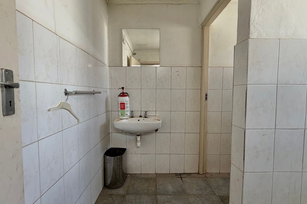 A basic industrial-style bathroom featuring a wall-mounted basin, tiled walls, and flooring, currently in need of refurbishment and modernization.