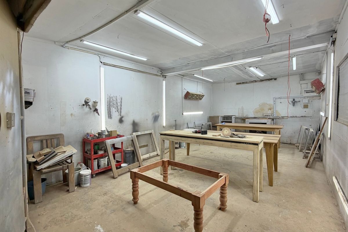 Industrial workshop space featuring concrete flooring, fluorescent lighting, and wall-mounted ventilation, suitable for various trade or manufacturing applications.