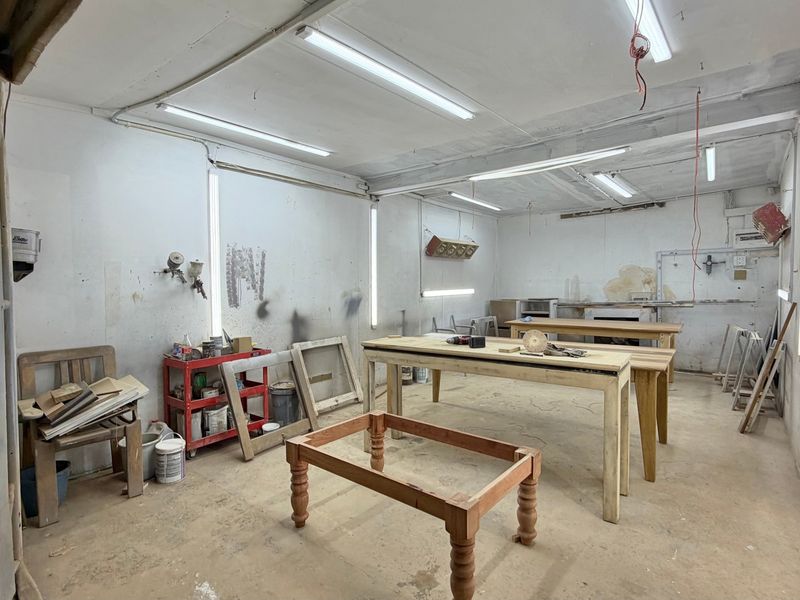 Industrial workshop space featuring concrete flooring, fluorescent lighting, and wall-mounted ventilation, suitable for various trade or manufacturing applications.
