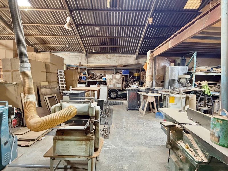 Industrial workshop space featuring high ceilings with exposed steel beams, corrugated metal roofing, and concrete flooring, equipped with built-in dust extraction infrastructure.
