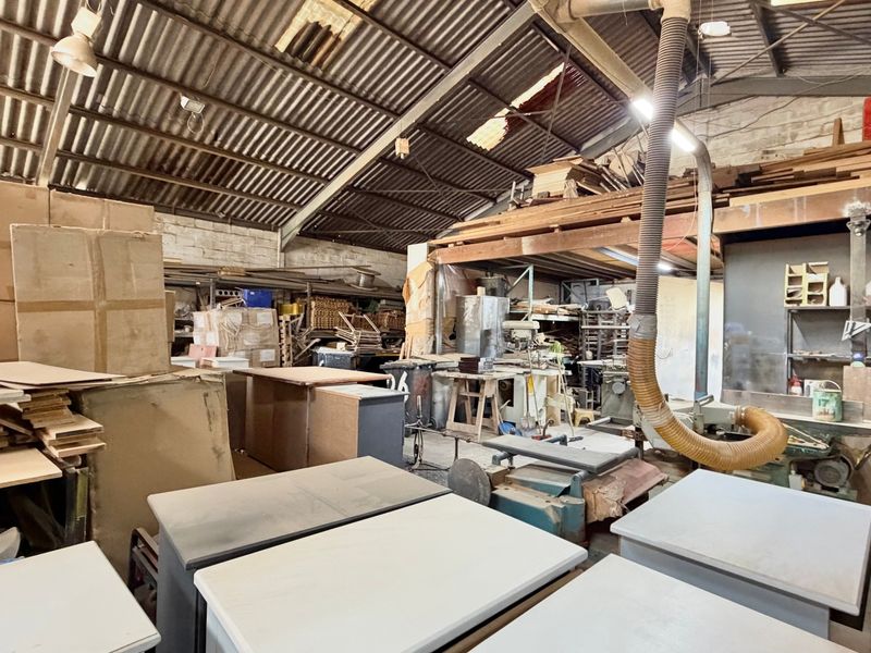 Industrial workshop space featuring high ceilings with exposed steel trusses, corrugated metal roofing, and an integrated dust extraction system.