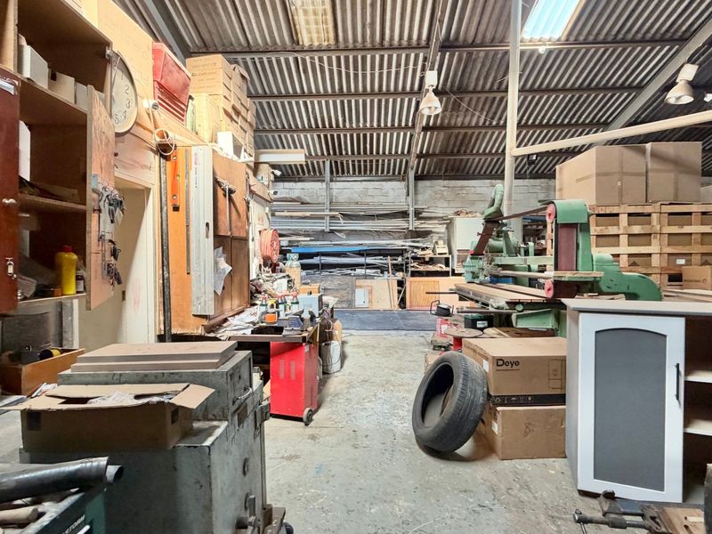 Industrial workshop space featuring high ceilings with exposed steel trusses, corrugated metal roofing, and durable concrete flooring, suitable for manufacturing or storage operations.