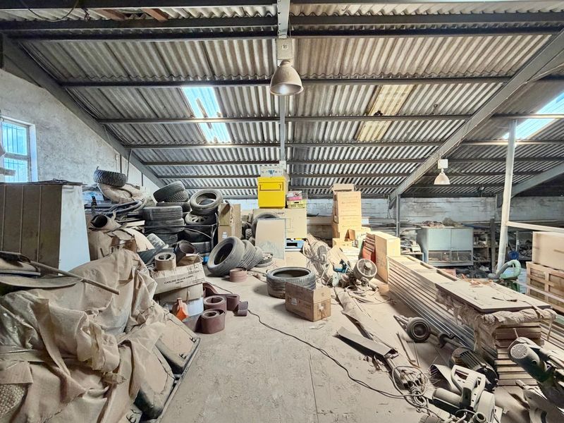 Spacious industrial utility area featuring exposed steel roof trusses, corrugated metal roofing, skylights, and concrete flooring, suitable for storage or workshop use.