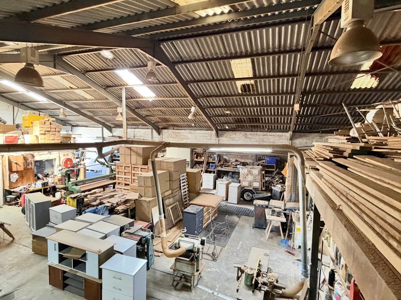 Spacious industrial workshop featuring high ceilings with exposed steel trusses, skylights, and integrated dust extraction systems, suitable for manufacturing or storage operations.