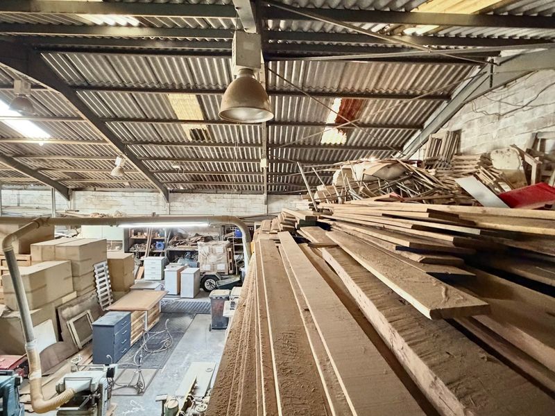 Industrial workshop space featuring high ceilings with exposed steel trusses, corrugated metal roofing, and industrial lighting, currently utilized for storage and manufacturing operations.