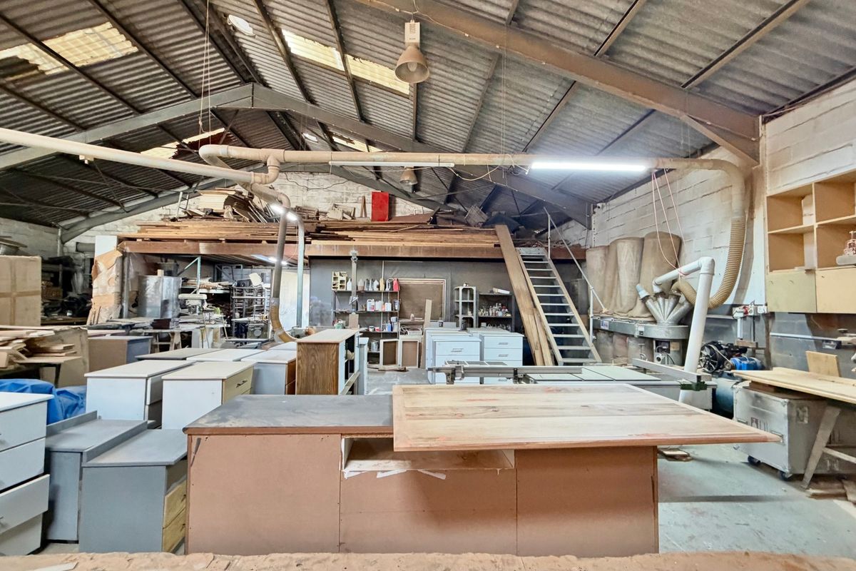 Industrial workshop space featuring high vaulted ceilings with exposed steel trusses, integrated dust extraction systems, a mezzanine level, and built-in storage shelving.