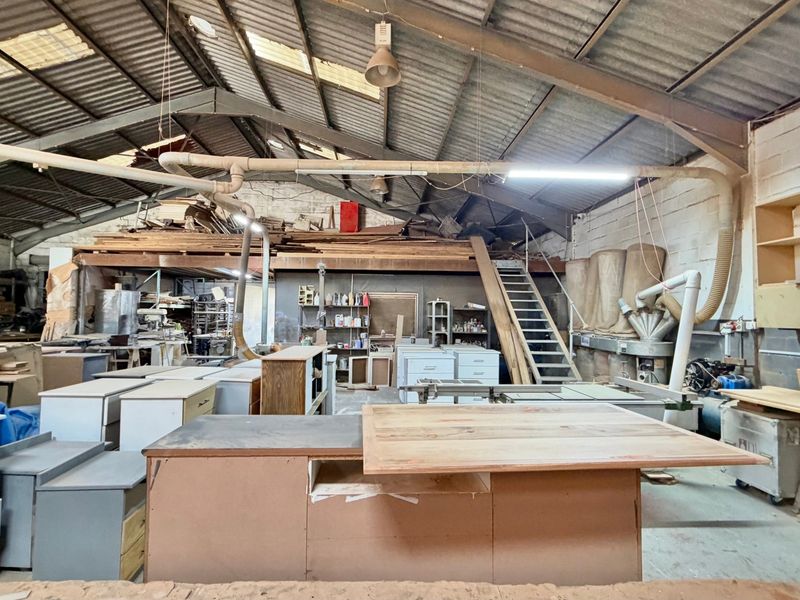 Industrial workshop space featuring high vaulted ceilings with exposed steel trusses, integrated dust extraction systems, a mezzanine level, and built-in storage shelving.