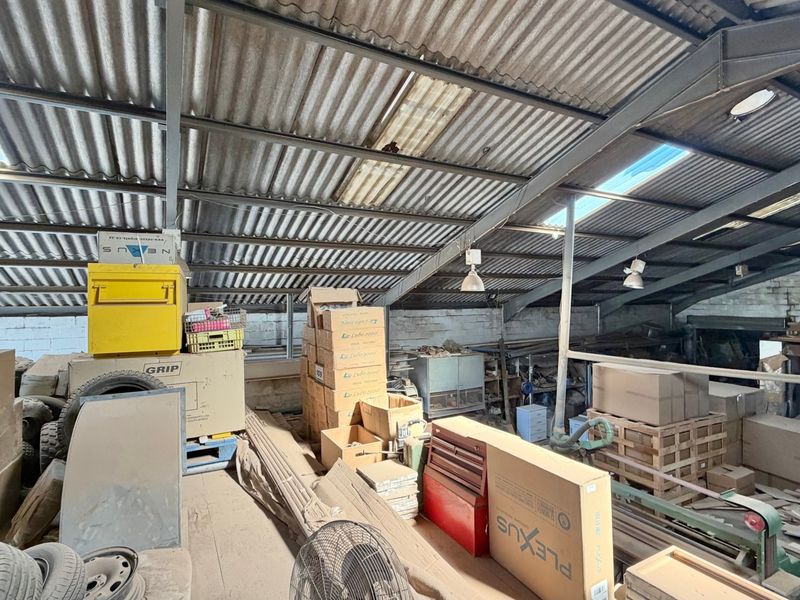 Industrial utility space featuring a high-pitched corrugated metal roof with integrated skylights, exposed steel structural trusses, and functional pendant lighting.