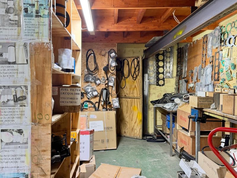 Industrial utility and storage space featuring exposed timber ceiling beams, steel structural elements, built-in plywood shelving units, and a functional workbench area.
