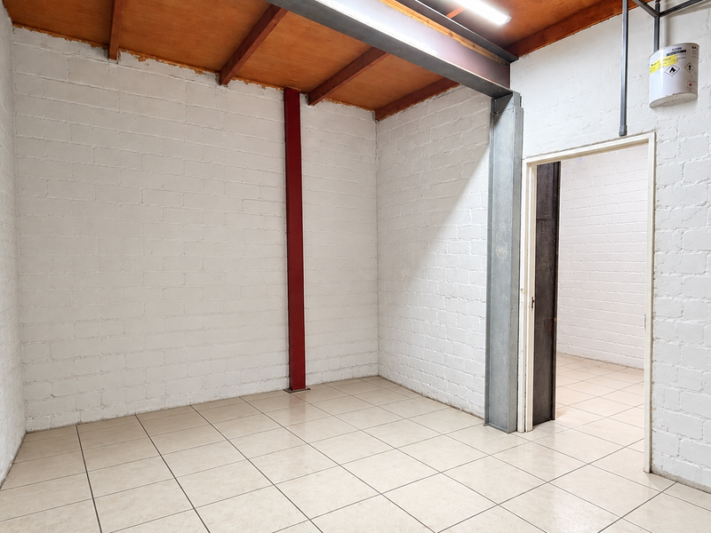 A clean, industrial-style utility space featuring exposed steel beams, timber ceiling, painted brick walls, and durable ceramic floor tiles.