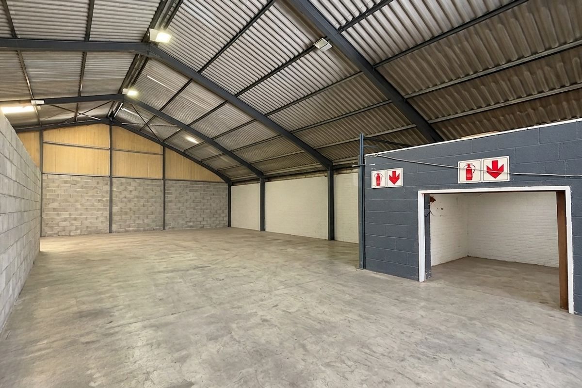 Spacious industrial warehouse unit featuring exposed steel portal framing, concrete flooring, and high-clearance corrugated metal roofing with integrated fire safety signage.