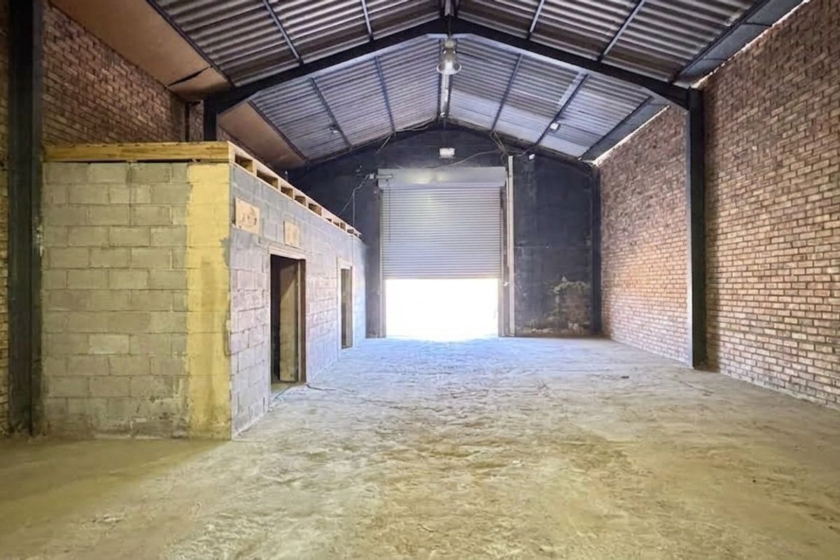 Spacious industrial warehouse unit featuring exposed brick walls, high-clearance steel portal frame, concrete flooring, and a large roller shutter door for vehicle access.