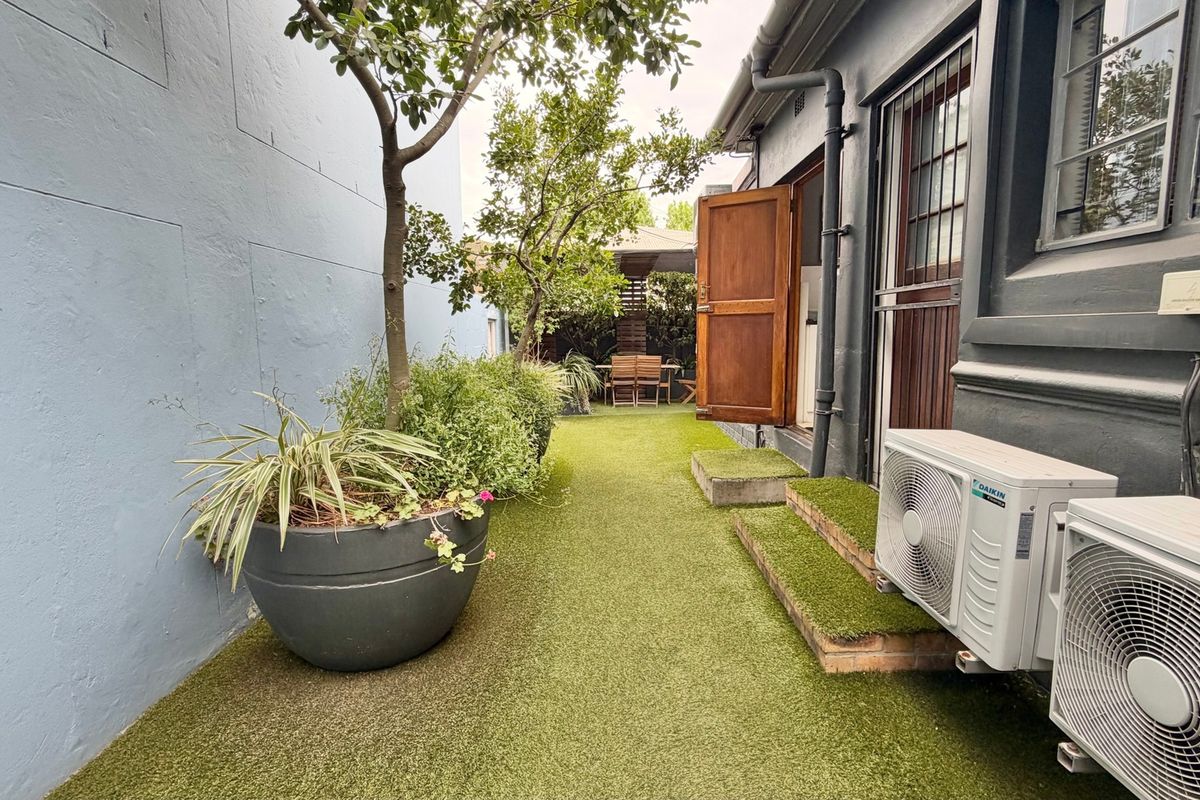 A narrow rear courtyard area featuring artificial turf, established trees, and external air conditioning units attached to the building exterior.