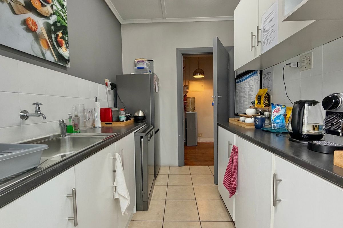 A functional galley-style kitchen featuring white cabinetry, dark laminate countertops, tiled flooring, and a tiled backsplash.