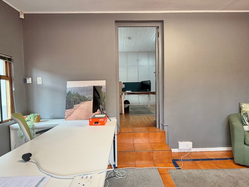 A functional office space featuring tiled steps leading to an adjacent room with built-in cabinetry and neutral wall finishes.