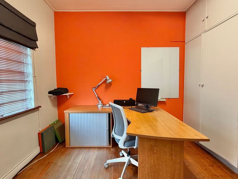 A functional office space featuring timber flooring, built-in storage cupboards, and a window with fitted blinds.