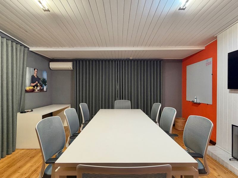A well-maintained professional meeting room featuring timber flooring, tongue and groove ceiling, integrated air conditioning, and a wall-mounted whiteboard.