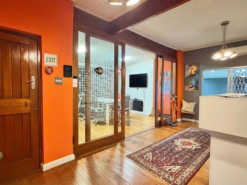A professional office reception area featuring timber flooring, a reception desk, and glass sliding doors leading into a partitioned meeting space.