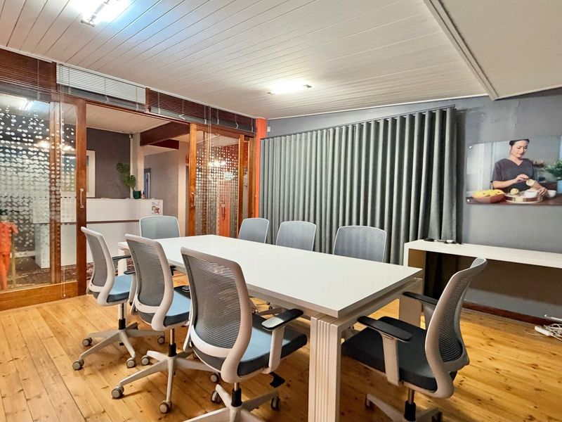A functional office meeting room featuring timber flooring, a tongue and groove ceiling, and glass-partitioned walls providing a professional workspace environment.