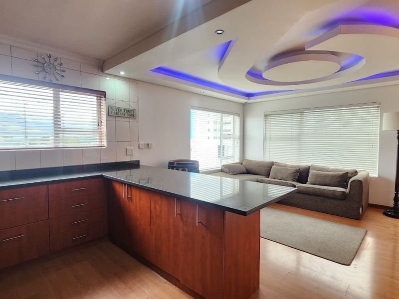 Spacious open-plan living area featuring a modern kitchen with granite countertops, wooden cabinetry, and a distinctive recessed ceiling with integrated LED lighting.