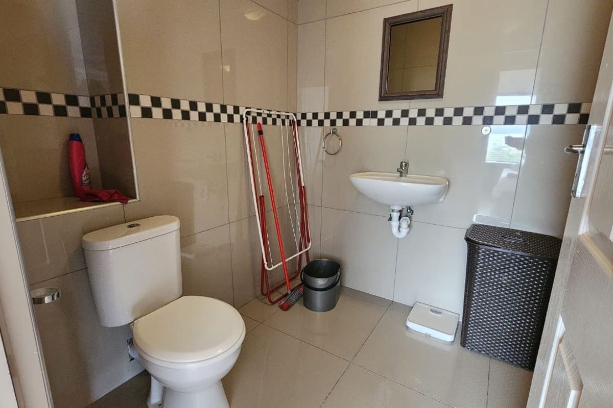A functional bathroom featuring tiled walls with a decorative border, a wall-mounted basin, and a standard toilet.