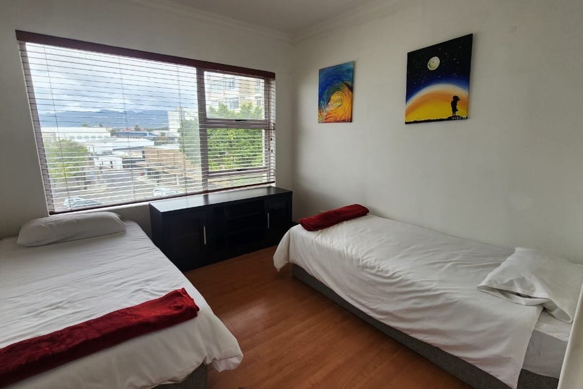 A bedroom featuring laminate flooring and large windows with venetian blinds, offering natural light and an urban view.