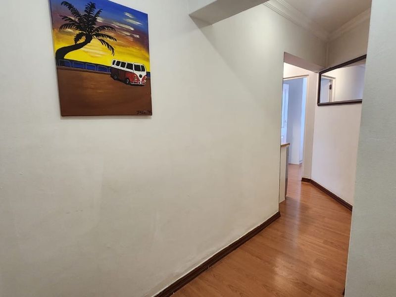 A clean and simple hallway featuring laminate wood flooring, neutral walls, and classic cornice detailing, providing a functional transition space within the apartment.