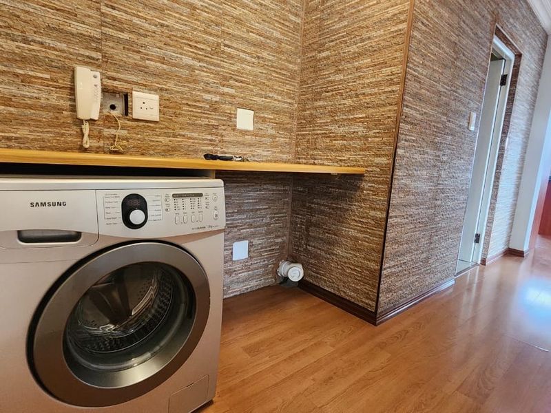 A functional laundry area featuring laminate flooring, stone veneer wall cladding, and a built-in counter with plumbing connections for a washing machine.