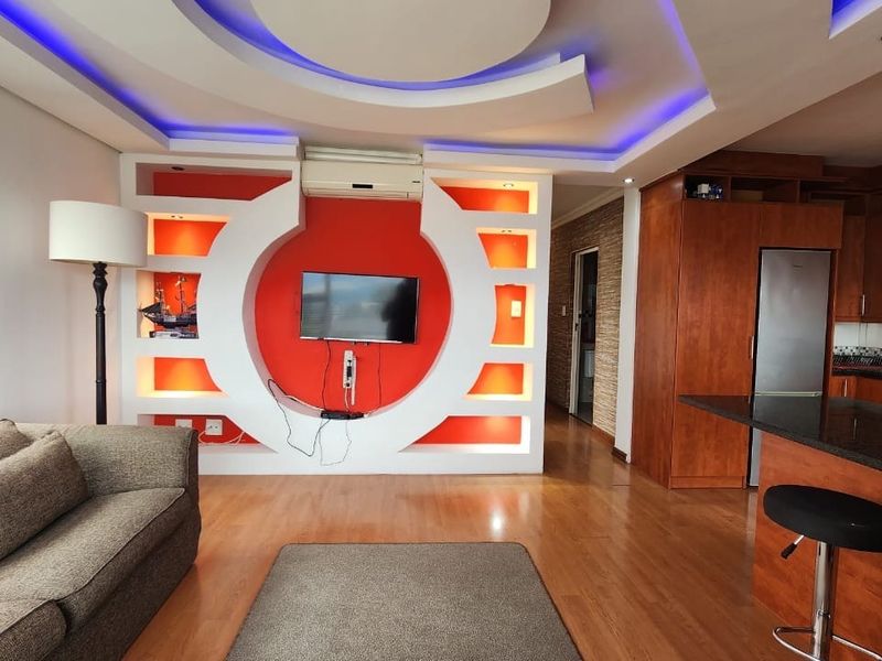 Open-plan living and kitchen area featuring a custom built-in media wall with integrated lighting, wooden cabinetry, and granite countertops.
