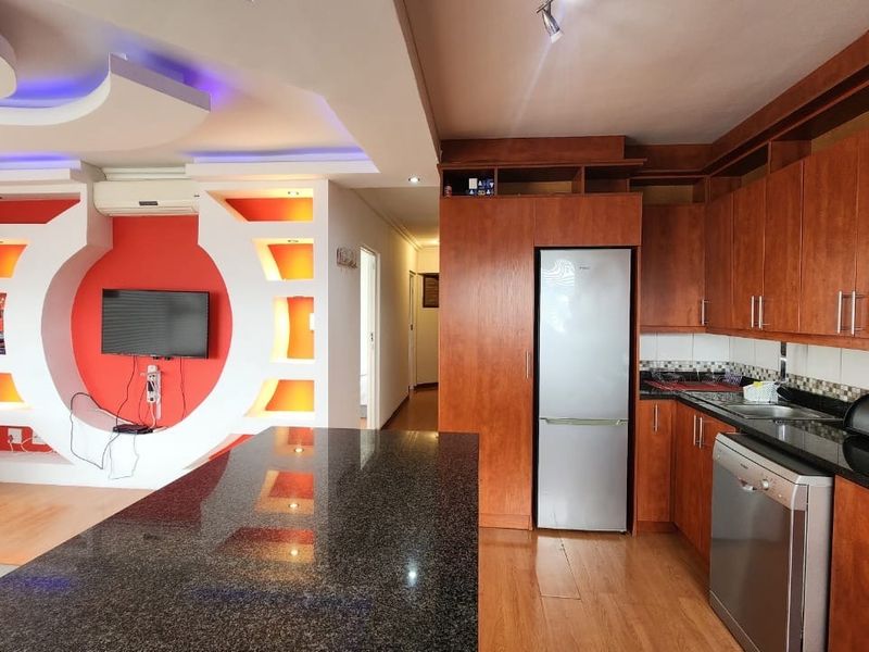 Open-plan living and kitchen area featuring granite countertops, extensive built-in cabinetry, laminate flooring, and a decorative feature wall with integrated lighting.