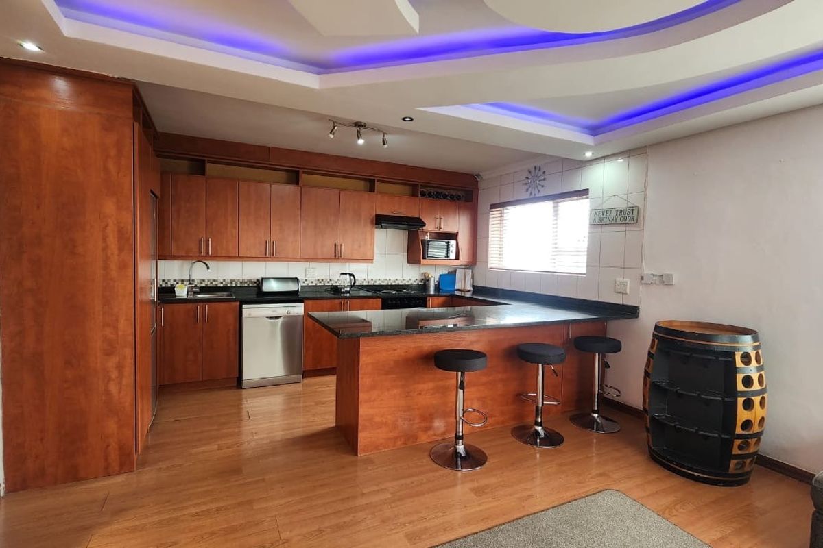 Open-plan kitchen featuring warm wooden cabinetry, granite countertops, a breakfast bar, and modern recessed ceiling lighting with integrated blue accent lighting.