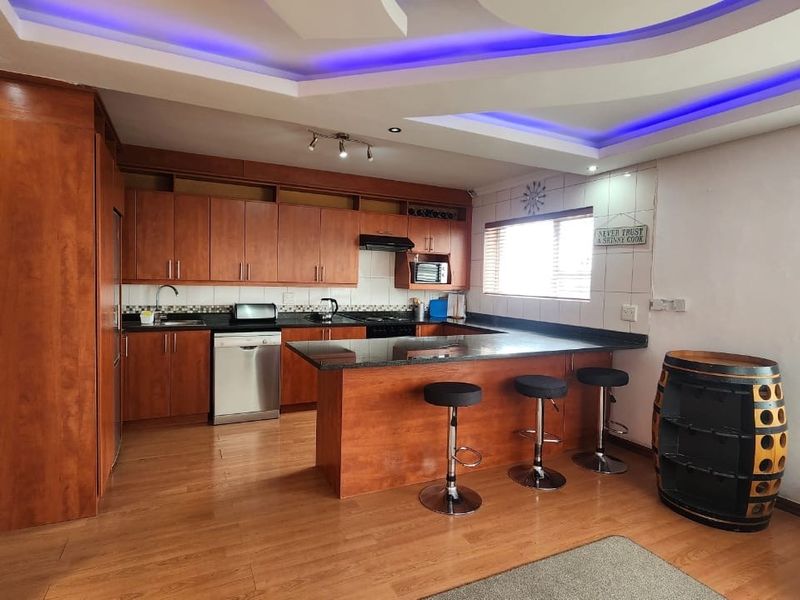 Open-plan kitchen featuring warm wooden cabinetry, granite countertops, a breakfast bar, and modern recessed ceiling lighting with integrated blue accent lighting.