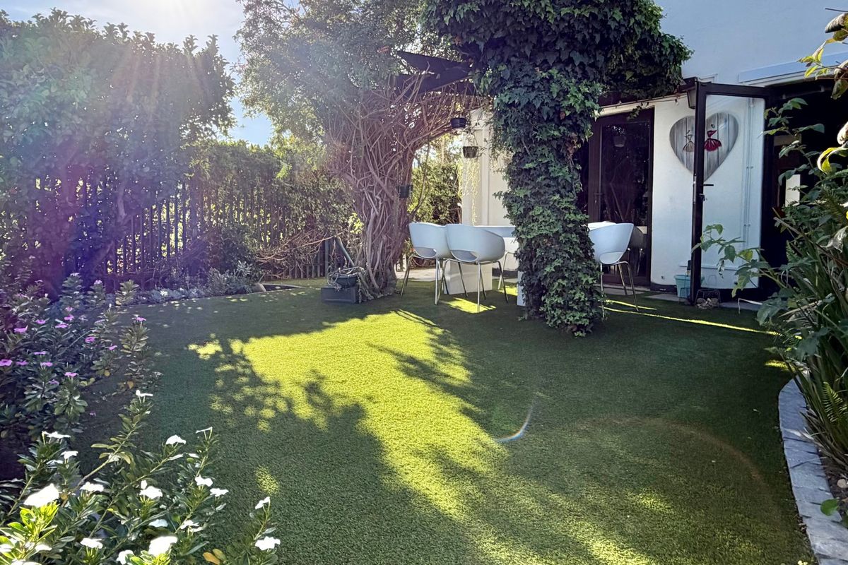 A private rear garden featuring an artificial lawn, mature trees, and a paved patio area accessible from the main living space.