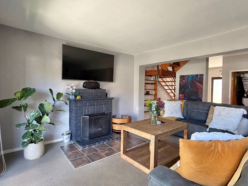 A living room featuring a brick fireplace, tiled hearth, and an open-plan staircase leading to the upper level, with access to an outdoor area.
