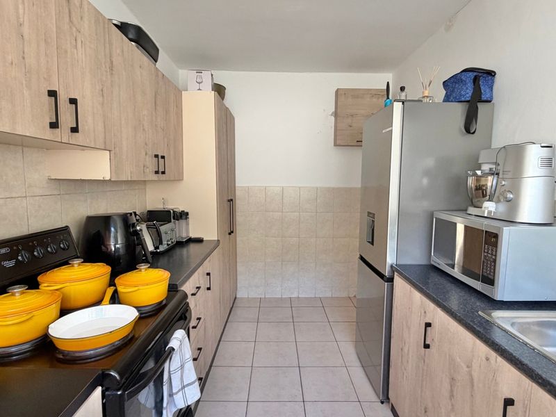 A functional kitchen featuring wood-look laminate cabinetry, tiled backsplash, and tiled flooring, providing a practical workspace with integrated stove and sink.