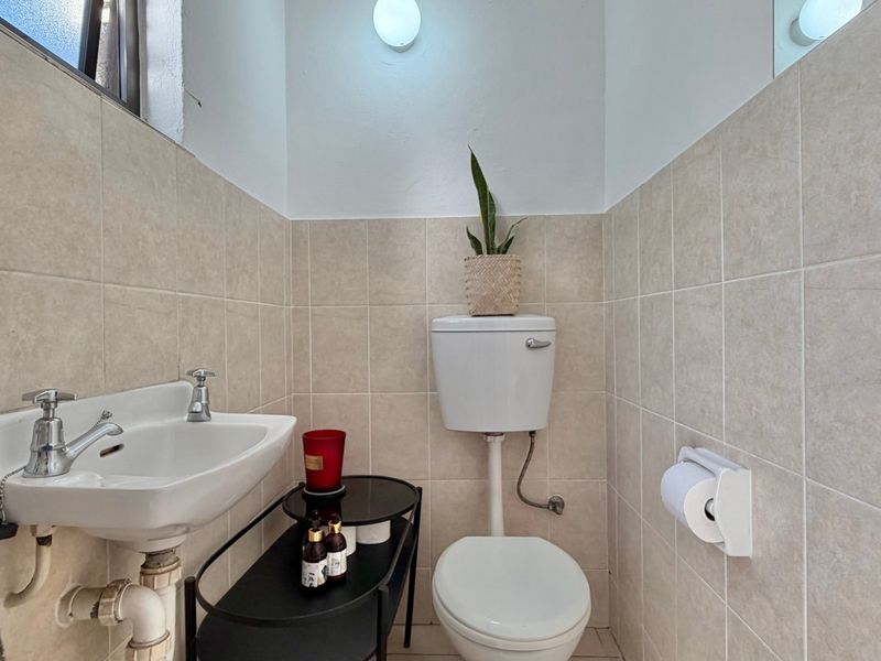 A compact guest bathroom featuring neutral ceramic wall tiles, a classic pedestal washbasin, and a standard toilet.