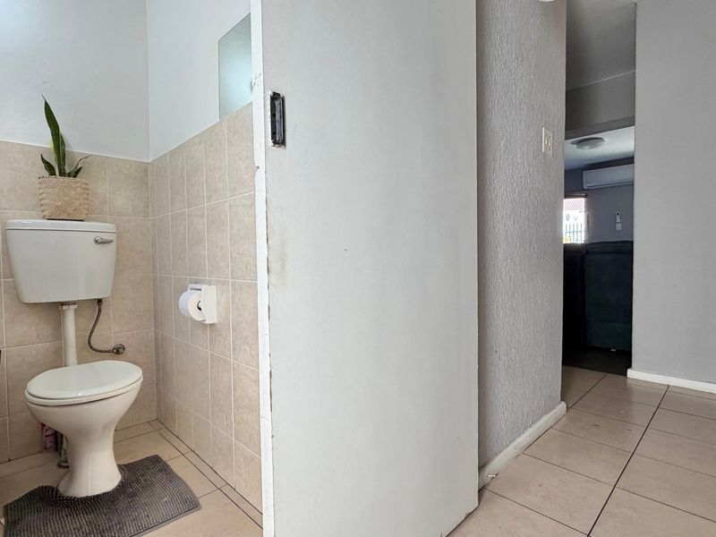 A functional bathroom featuring ceramic wall and floor tiling, equipped with a standard toilet and situated adjacent to a hallway.