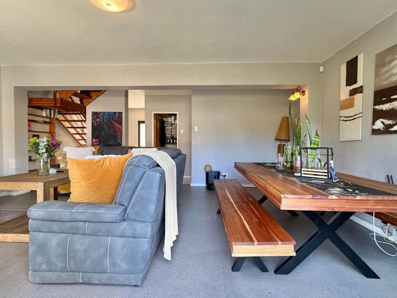 Spacious open-plan living and dining area featuring tiled flooring, a built-in fireplace, and a wooden staircase leading to the upper level.