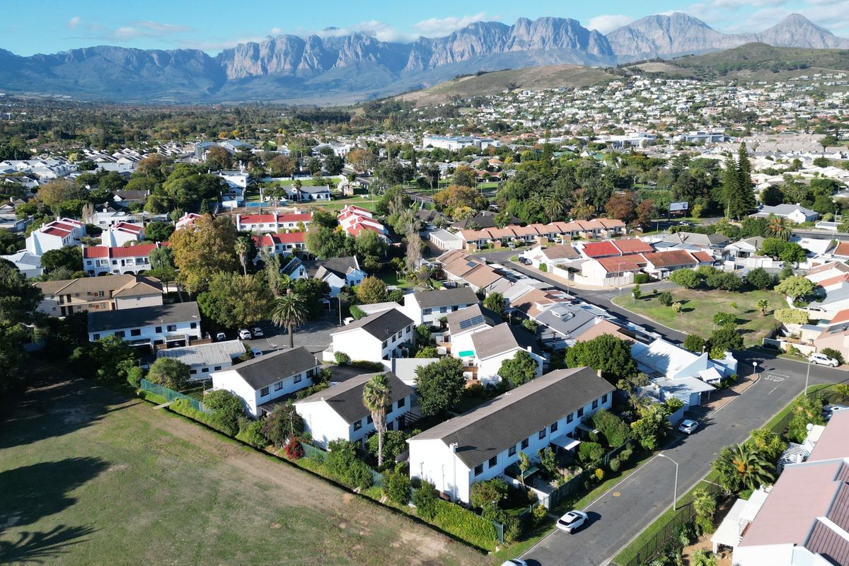 An aerial view of a residential townhouse complex featuring multiple units, paved streets, and landscaped surroundings with a mountain range in the background.
