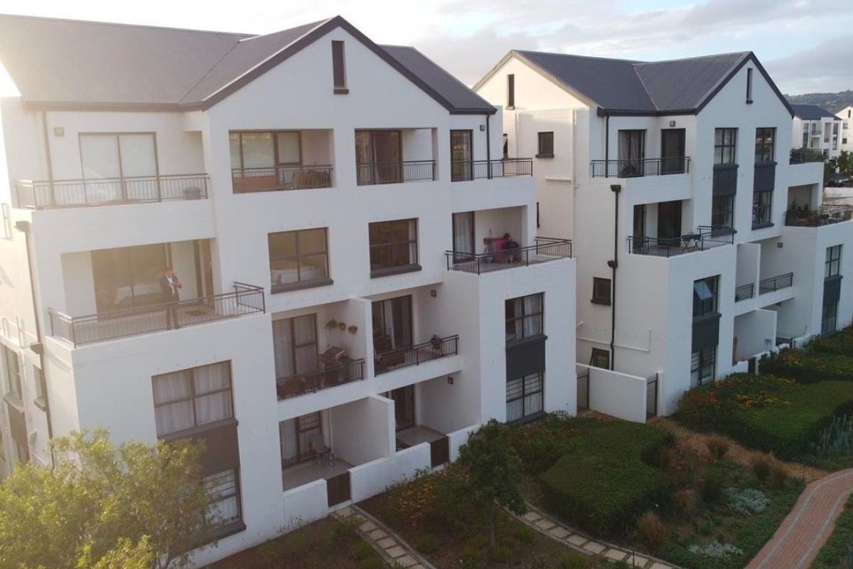 Aerial view of a modern apartment complex featuring multi-story buildings with private balconies, pitched roofs, and well-maintained landscaped gardens with paved walkways.