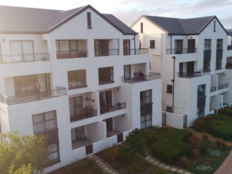 Aerial view of a modern apartment complex featuring multi-story buildings with private balconies, pitched roofs, and well-maintained landscaped gardens with paved walkways.