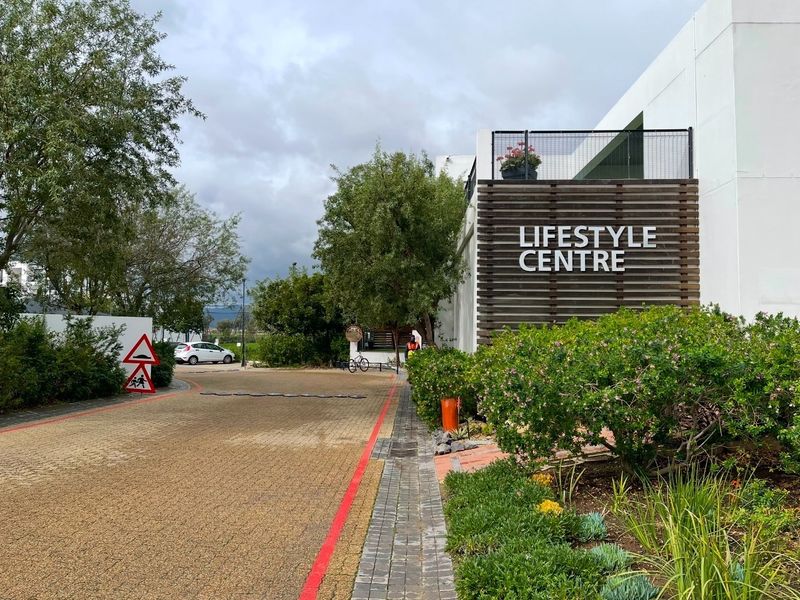 Exterior view of the apartment complex lifestyle centre featuring a paved driveway, landscaped gardens, and modern timber slat architectural detailing.