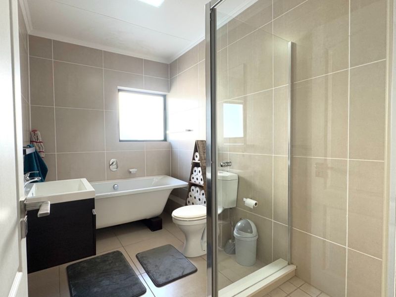Modern bathroom featuring a freestanding bathtub, separate glass-enclosed shower, vanity cabinet, and neutral wall tiling.