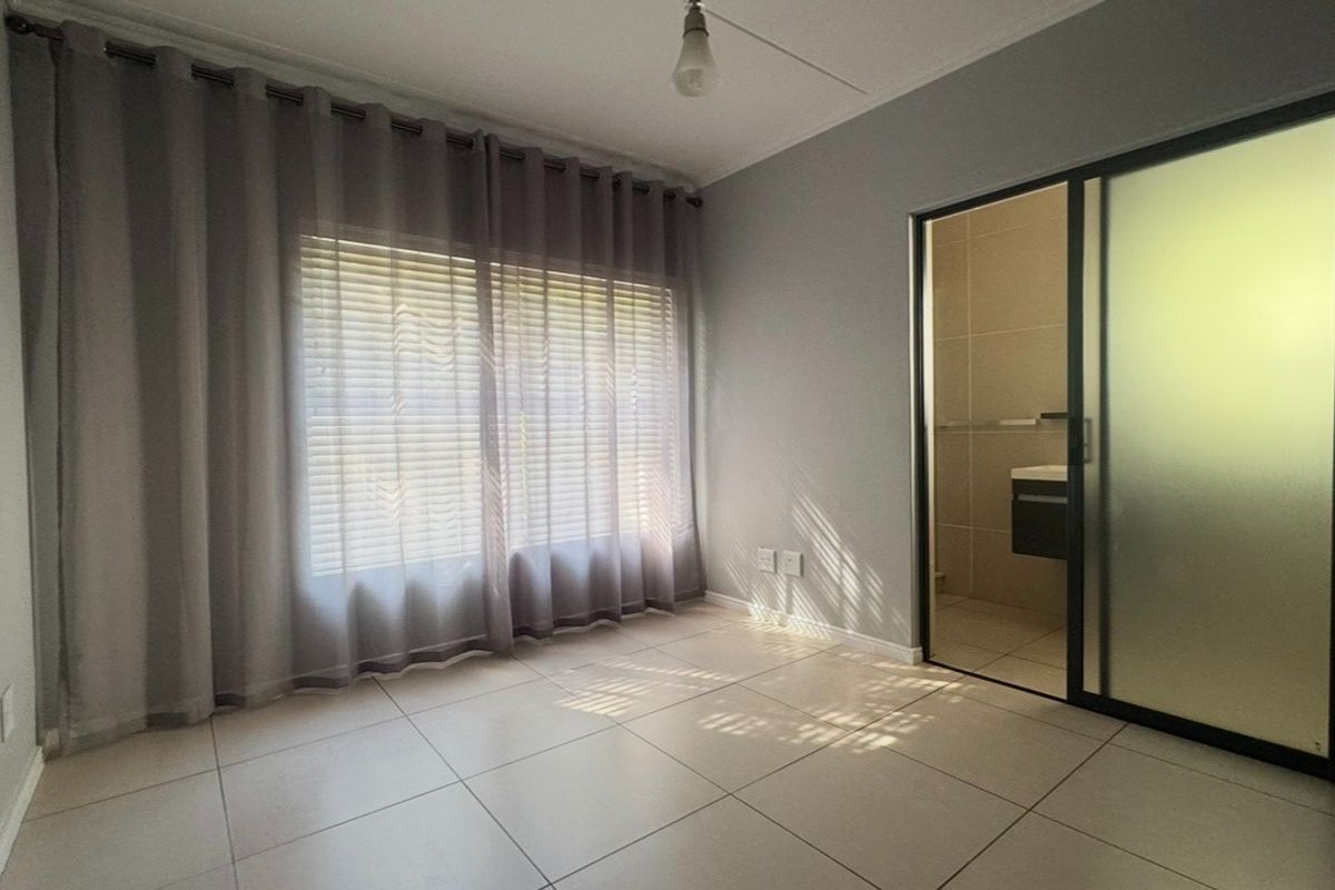 An empty bedroom featuring tiled flooring, large window with curtains, and an integrated sliding door leading to an en-suite bathroom.