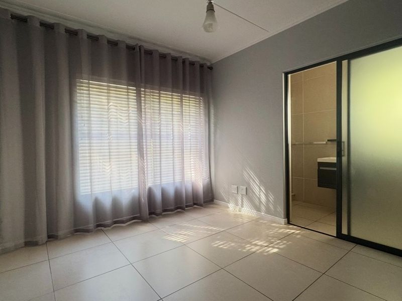 An empty bedroom featuring tiled flooring, large window with curtains, and an integrated sliding door leading to an en-suite bathroom.