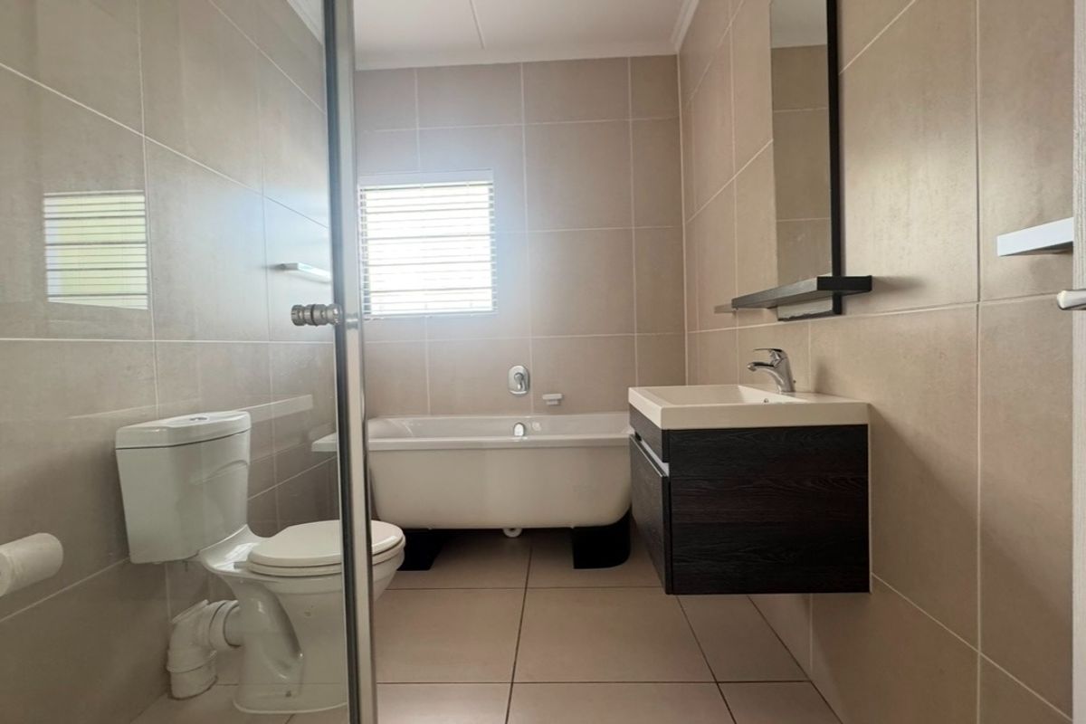 Modern bathroom featuring a freestanding bathtub, wall-mounted vanity, glass shower enclosure, and neutral floor-to-ceiling tiling.